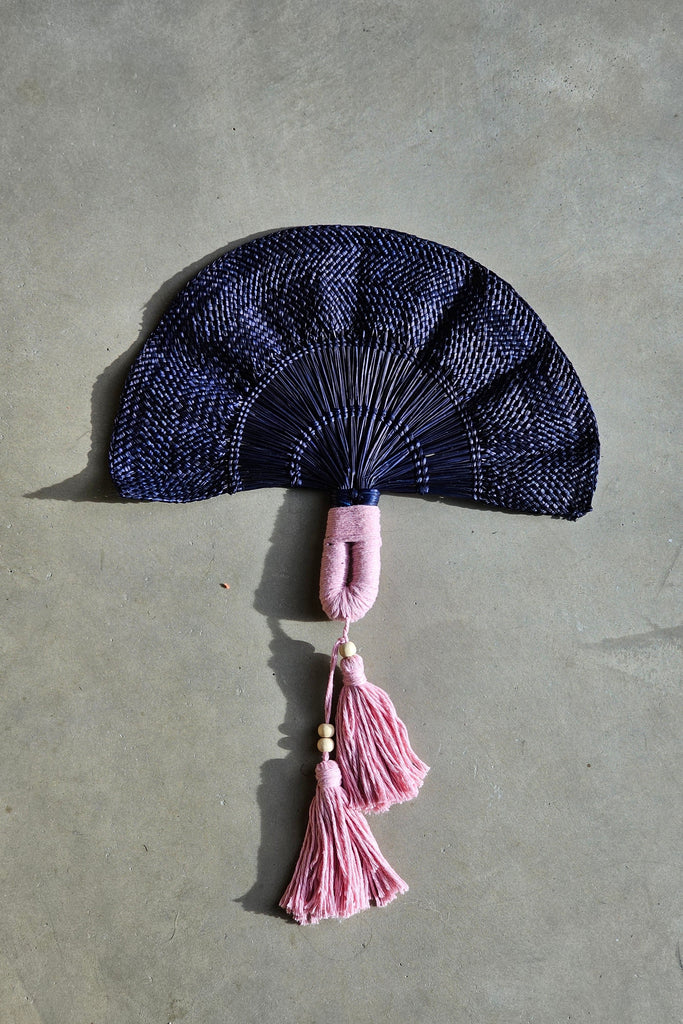 Abanico de la marca Caraná hecho a mano en iraca por artesanos colombianos en color azul oscuro con flecos rosados