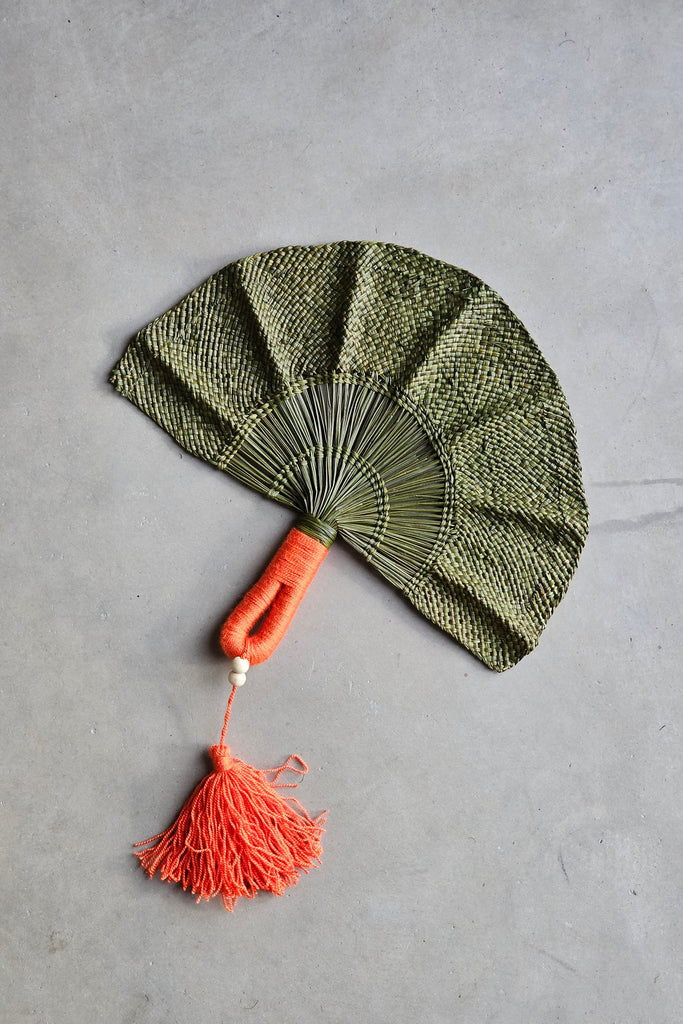 Abanico de la marca Caraná hecho a mano en iraca por artesanos colombianos en color verde con flecos naranjados